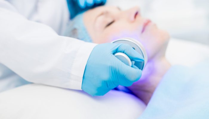 Gloved cosmetician holding electric device while making beauty procedure on client face