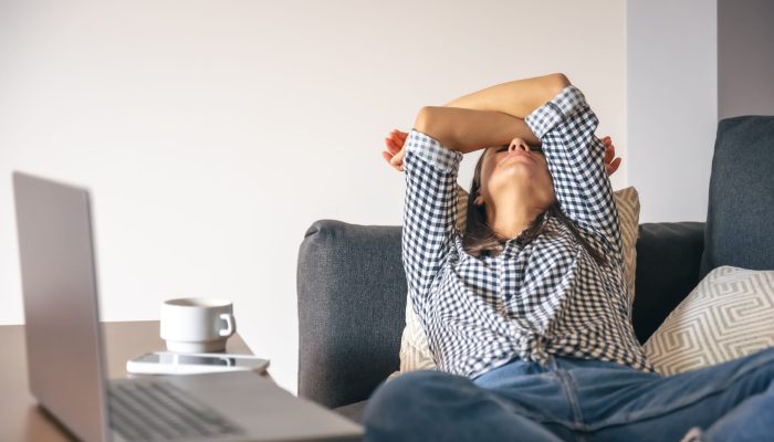 Tired from work, a young woman with a laptop lies on the couch.