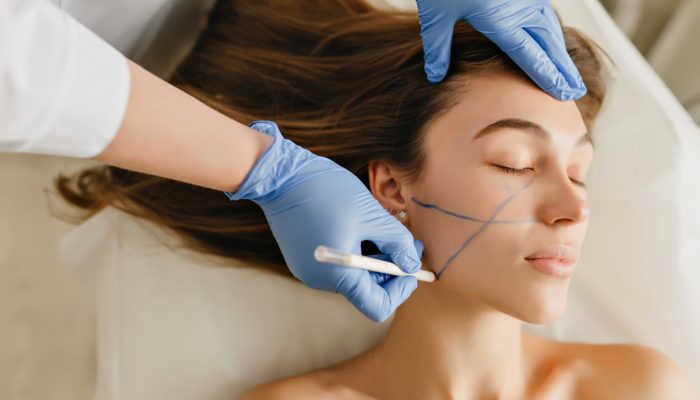 Closeup portrait beautiful woman during cosmetology procedures, rejuvenation in beauty salon. Dermatology procedure , painting eyebrows, hands in blue glows, at work, healthcare, botox