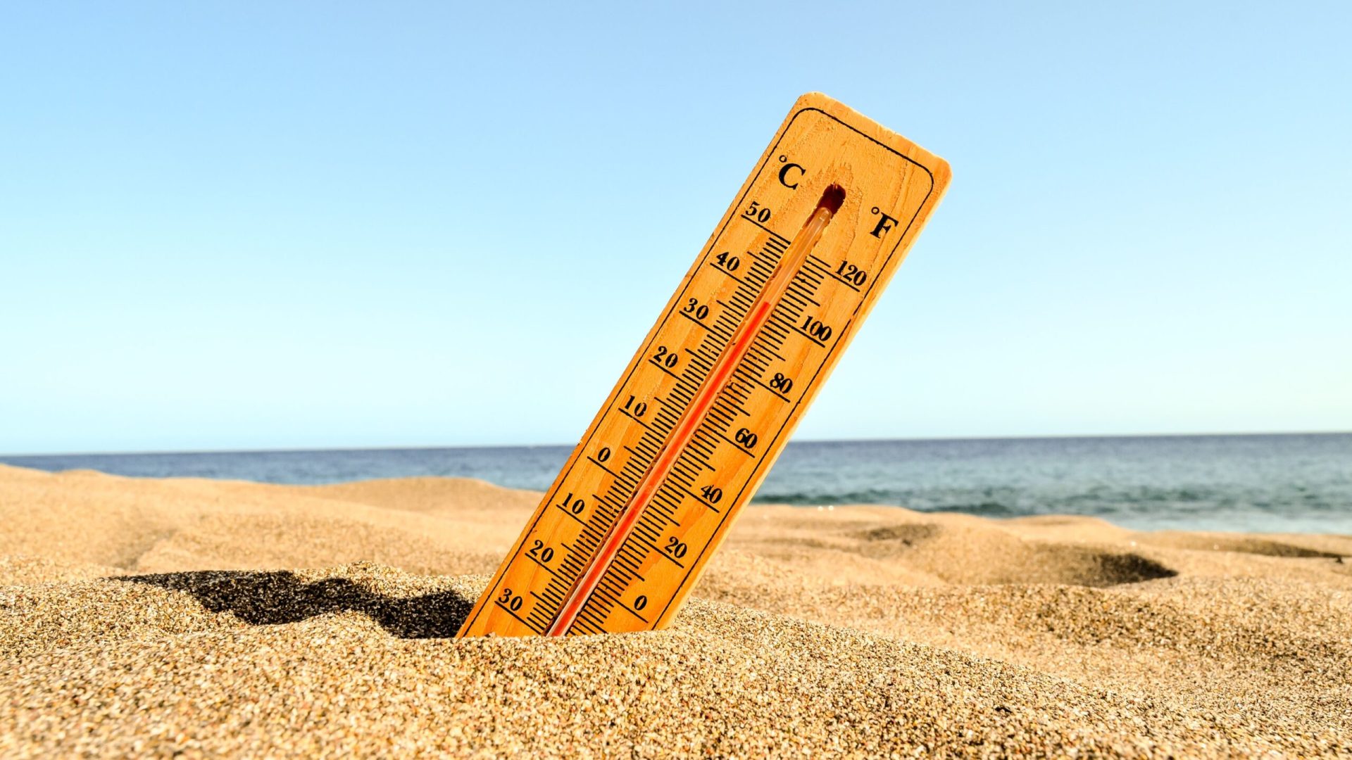 A selective focus shot of a thermometer in the beach sand with a blurred background