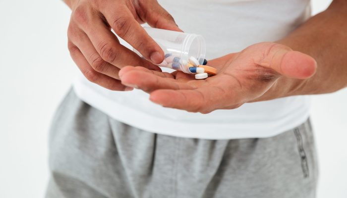 Cropped picture of young sportsman standing over white background holding vitamins and sport pills.