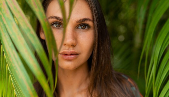 Close Graceful Woman model in  red  swim wear with long straight hair posing   in tropical nature.