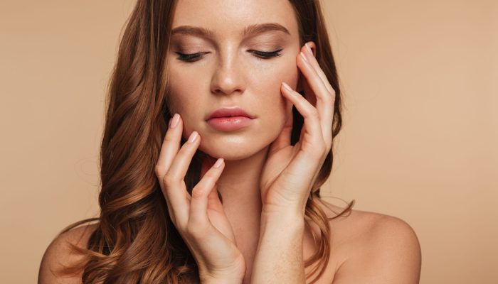 Close up Beauty portrait of sensual ginger woman with long hair posing with arms near the face over cream background
