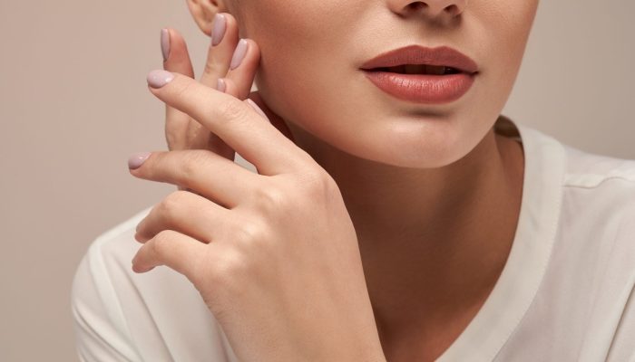 Crop of young female model with perfect makeup presenting minimalistic silver bracelet. Portrait of woman looking at camera in studio, isolated on gray background. Concept of jewelery.