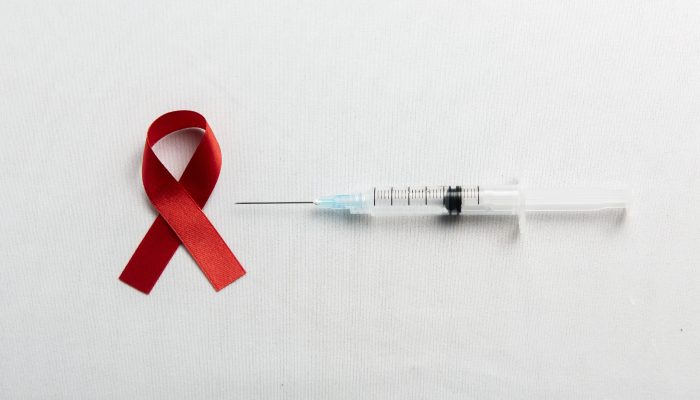Red ribbon and syringe with white background. Hiv Aids ribbon awareness