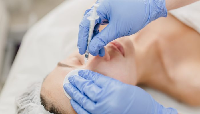 Hands in blue glows of cosmetologist at work with pretty woman during injection on face. Rejuvenation, professional, healthcare, medicine, medical therapy, skincare, botox
