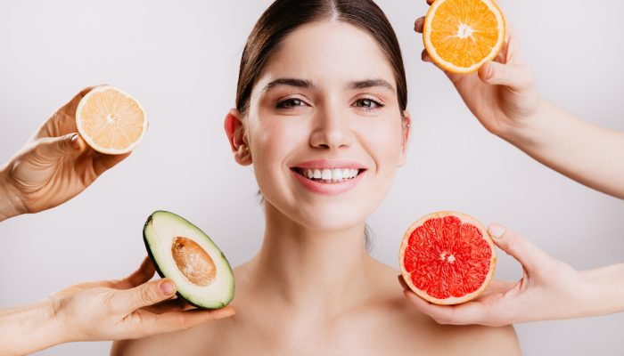 Healthy beautiful radiant skin of woman without makeup. Portrait of girl smiling against background of fruits