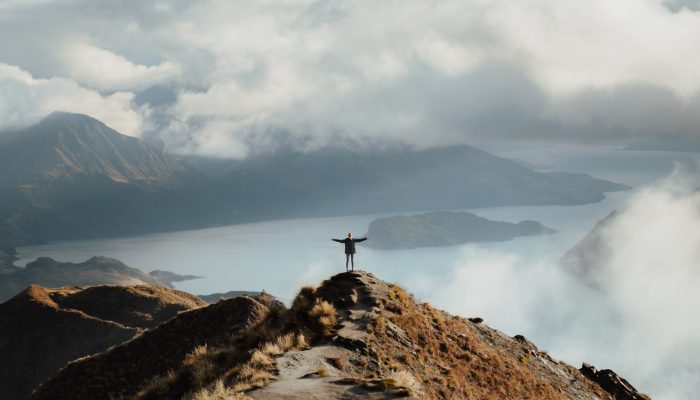 A man with hands wide open standing at the top of a mountain enjoying the incredible view of a lake