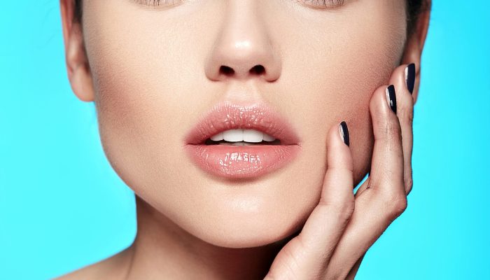 Glamor closeup beauty portrait of beautiful sensual Caucasian young woman model with nude makeup  touching her perfect clean skin isolated on blue background