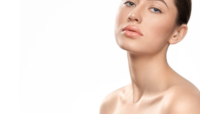 Pretty, stylish model with bare shoulders on white isolated background. Attractive girl with beautiful make up, perfect healthy skin, plump lips posing and looking at camera.