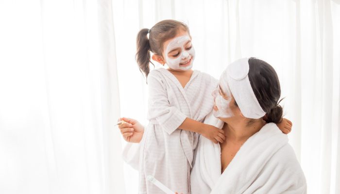 A mother and her young pretty daughter having fun in the bedroom and making clay facial masks