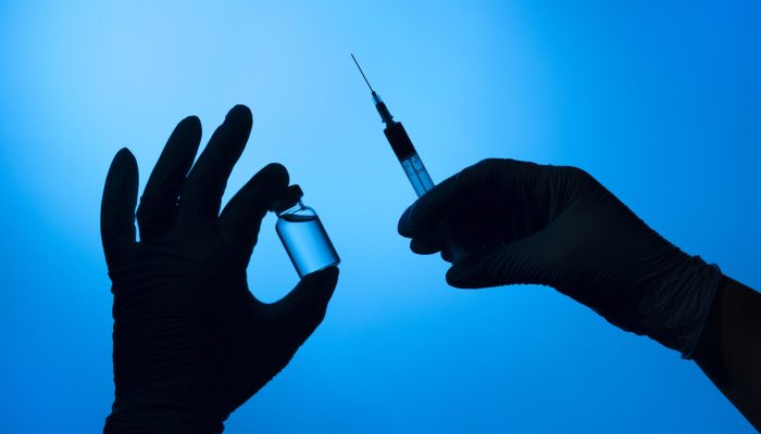 maos-com-luvas-de-protecao-segurando-uma-vacina-covid