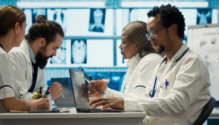 Physicians examining x ray scan results in a meeting with the staff, working to develop treatment plans. Doctors doing collective work for diagnostics control, healthcare industry. Camera A.