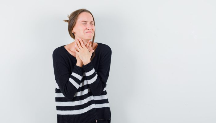 young woman having sore throat in striped knitwear and black pants and looking exhausted. front view.