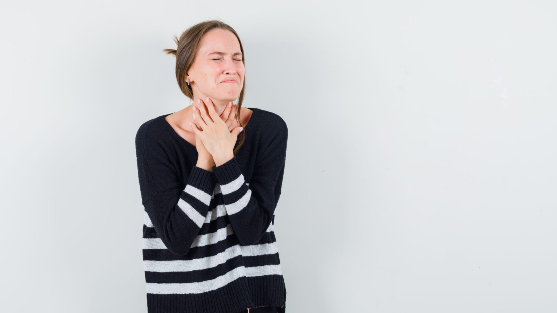 young woman having sore throat in striped knitwear and black pants and looking exhausted. front view.