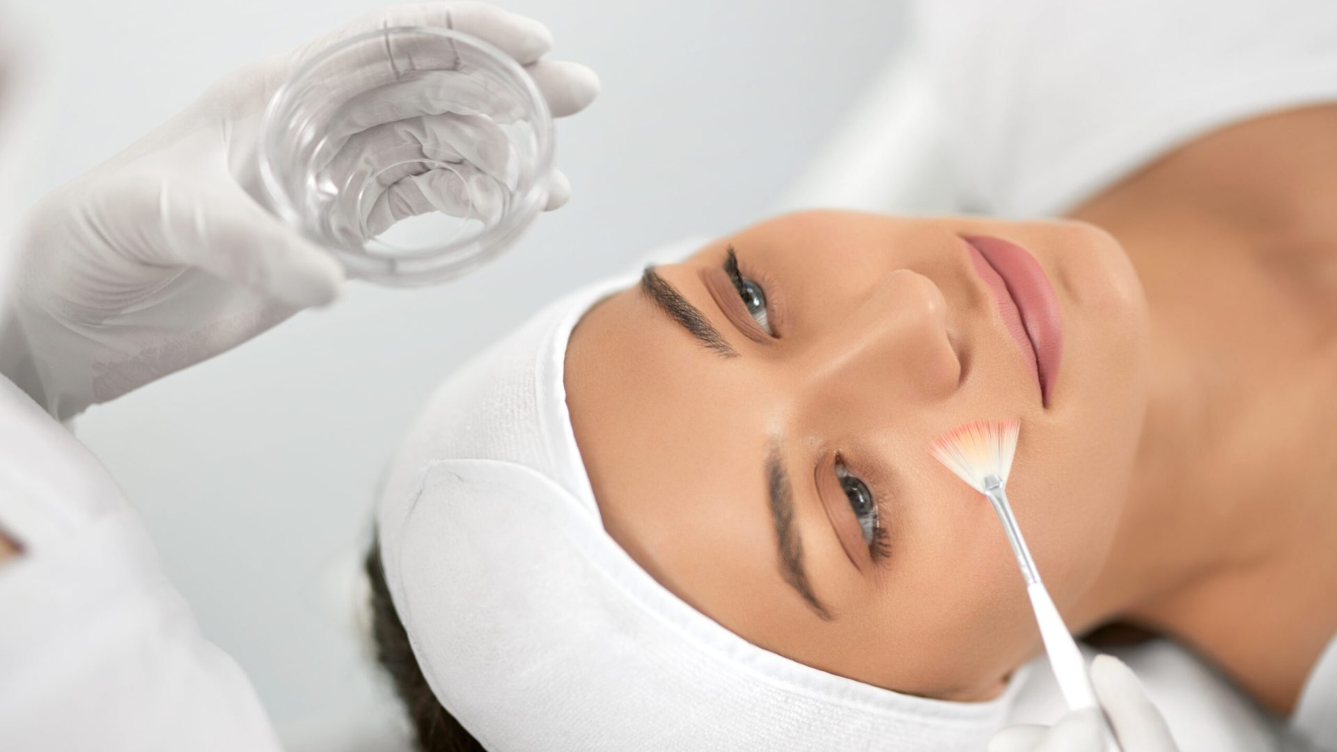 Top view portrait of beautician holding special masks for face and doing peeling for young beautiful woman. Concept of improvements skin with special cosmetic procedure in beauty salon.