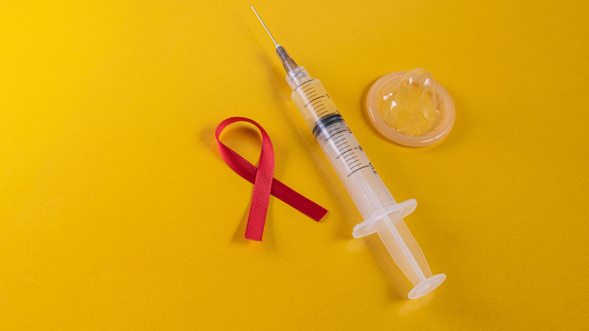 Red ribbon latex condom and syringe on the blue background