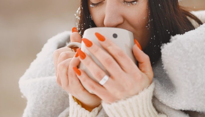 Close-up portrait of woman in white sweater. Woman standing in snowy day. Girl with tea.