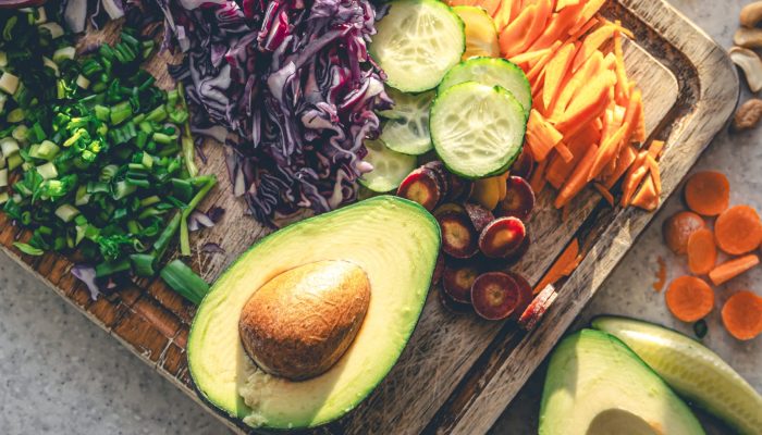Sliced fresh vegetables on a cutting board on the kitchen table, top view. Avocado and other vegetables in the process of preparing the salad. The concept of healthy eating and vegetarianism.