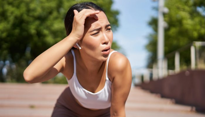 Tired young female runner, asian girl taking break during workout, stop jogging, panting while breathing, running in park.