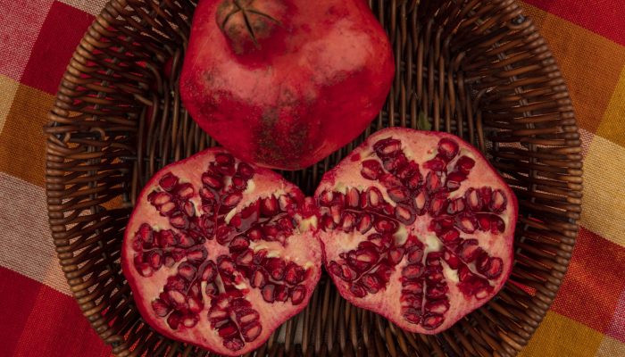 top view of fresh red and juicy pomegranates on a bucket on a checked cloth on a grey background