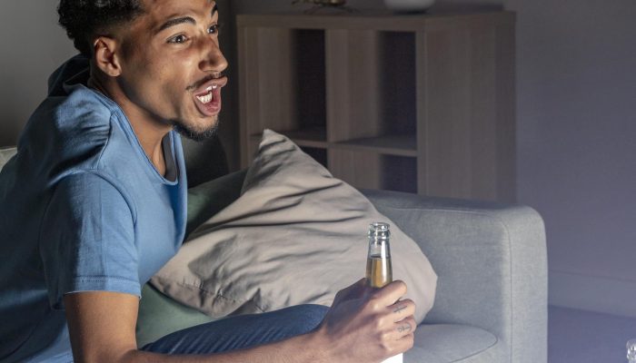 vista-lateral-de-um-homem-torcendo-para-tv-em-casa-com-cerveja-e-petiscos