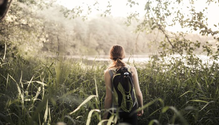 vista-traseira-de-femininas-hiker-andar-em-grama-verde