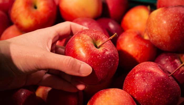 Close-up, an apple in a woman's hand, a selection of fruits in a supermarket.