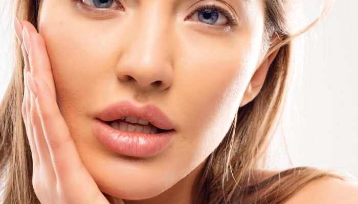 wonderful-lady-with-beautiful-face-big-lips-white-teeth-blue-eyes-soft-skin-hand-cheek-manicure-volume-blonde-hair-modern-natural-makeup-white-clothes