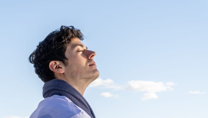 Portrait of young boy with head to the sky and eyes closed on a clear day with blue sky and some white cloud